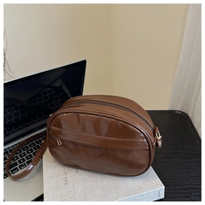 Detail of glossy brown faux leather crossbody bag with gold-tone hardware and top zipper