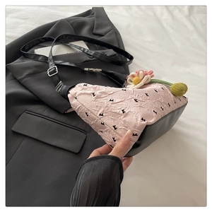 Detail of pink pleated fabric crossbody bag with floral charms and black leather base