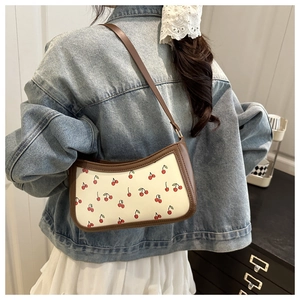 Détail du sac sous l'aisselle rétro à imprimé cerise porté par un mannequin en jean