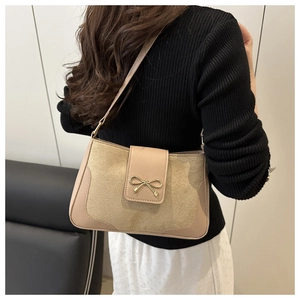 Detail of beige shoulder bag featuring a golden bow metal clasp and textured fabric
