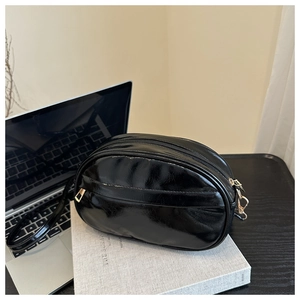 Detail of black glossy oval crossbody bag with gold zippers on a white book base