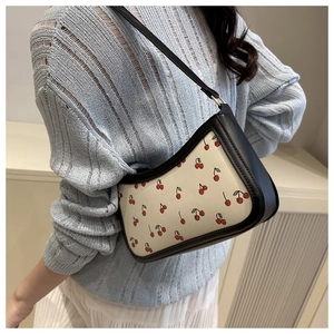 Détail d'un sac à bandoulière demi-lune avec imprimé cerises et finitions en cuir noir