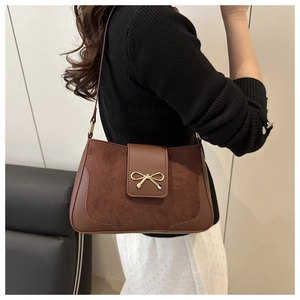 Close-up of brown crossbody bag featuring suede patchwork and a gold bow clasp detail