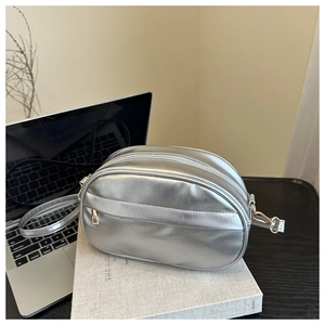 Detail of silver oval shoulder bag with metallic PU texture and dual zippers on a book