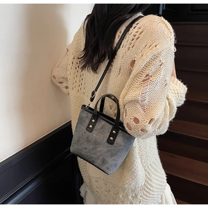 Back view of a grey suede bucket bag with gold studs and a black adjustable strap