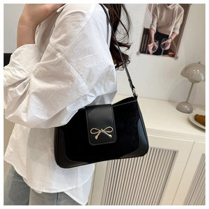 Detail of black crossbody bag featuring a golden bow buckle and mixed textures