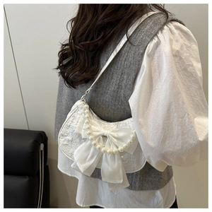 Detail of white lace handbag featuring a pearl handle and large silk bow decoration