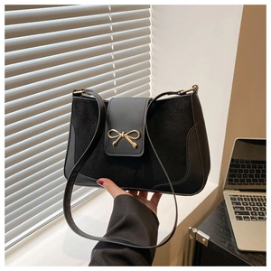 Close-up of black matte leather shoulder bag with a stylish metal bow buckle detail