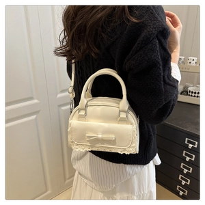 Detail of cream bowling bag featuring bow tie ornament and delicate lace trim edge
