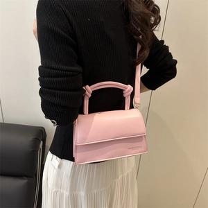 Pink minimalist leather square bag with twisted handle shown on model in modern style