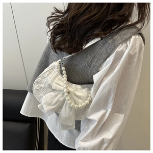 Detail view of a white lace shoulder bag with a silk bow and decorative pearl chain strap
