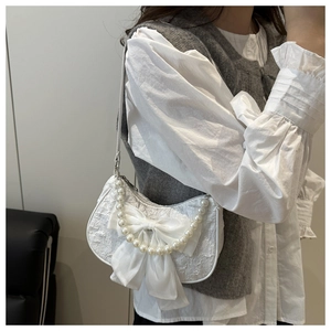 Detail view of a white textured underarm bag featuring a large bow and pearl strap