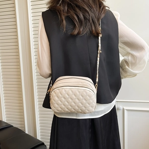 Beige quilted chain crossbody bag shown on model with dual zippers and sleek texture