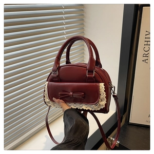 Close-up of burgundy bowling bag with beige lace trim and central leather bow detail