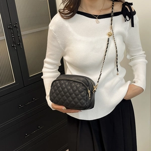 Elegant black quilted crossbody bag with gold metal ball and leather chain strap on model