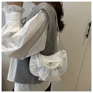 Detail of white lace shoulder bag featuring pearl strap and large bow decoration