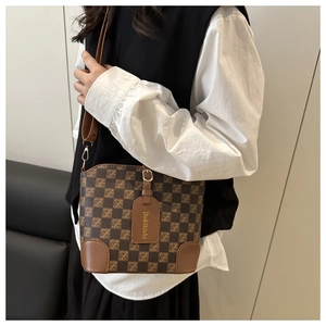 Macro detail of brown checkered bucket bag with leather edges and adjustable strap
