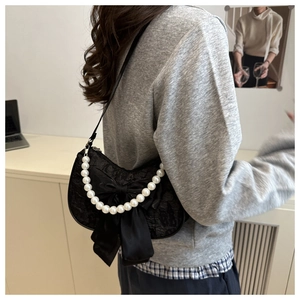Detail of black lace shoulder bag featuring oversized bow and elegant pearl handle