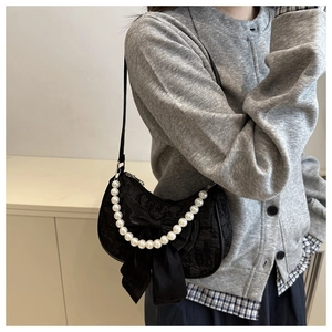 Detailed shot of a black lace bow shoulder bag with pearls on a female model