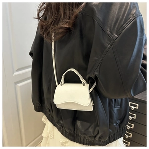 Détail du mini sac blanc gaufré crocodile porté avec une veste en cuir élégante