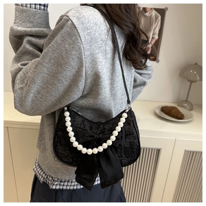 Detail of black lace shoulder bag with large satin bow and elegant pearl chain strap