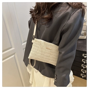 Detail of beige straw crossbody bag featuring herringbone weave and metal plate accent