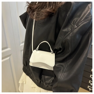 Détail d'un mini sac blanc à motif crocodile porté sur une veste en cuir noir stylée