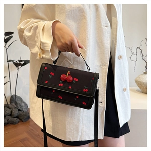 Detail of a black crossbody bag with cherry prints and 3D cherry buckle detail