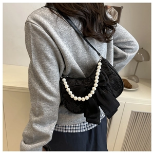 Detail of black lace shoulder bag featuring a large mesh bow and elegant pearl chain strap