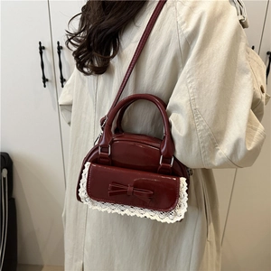 Borsa bowling bordeaux lucida con fiocco e bordo bianco, indossata da una modella donna