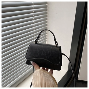 Détail d'un sac à main noir texture crocodile avec rabat ondulé et boucles argentées