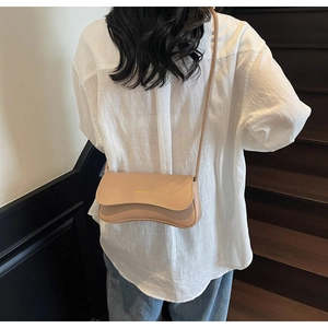Detail view of a tan leather crossbody bag shown on model against a wooden staircase