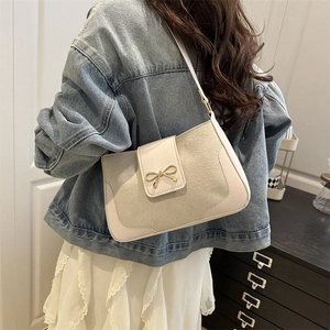 Minimalist off-white crossbody bag with gold bow clasp worn with a denim jacket