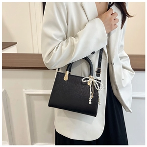 Detail of a chic black square crossbody bag featuring a pearl bow charm and gold hardware
