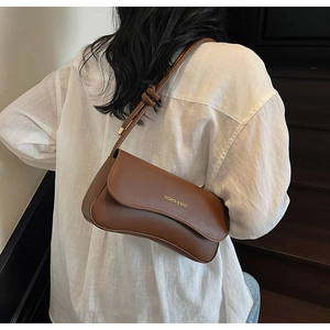 Detail of caramel brown leather underarm bag with knot strap and gold metal accents