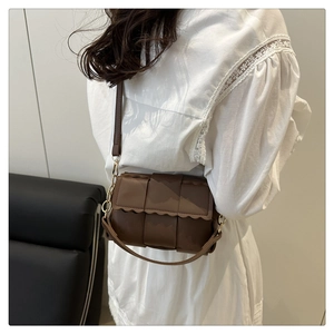 Detail of a brown woven crossbody bag featuring scalloped edges and gold hardware on model