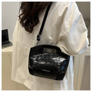 Detail of glossy black patent leather bucket bag with silver metal hooks and shoulder strap