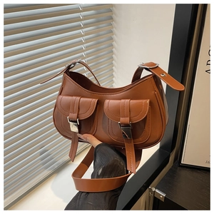 Detail of brown leather crescent bag featuring dual front pockets and silver metal buckles