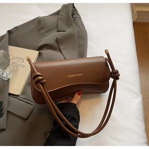 Detail of a brown leather shoulder bag with gold lettering and a knotted cylinder strap