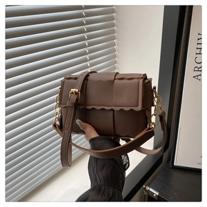 Close-up of woven dark brown leather crossbody bag with scalloped edges and gold chain