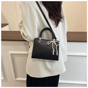 Side view of black pebble leather handbag with pearl bow charm and gold hardware