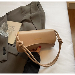 Detail of beige shoulder bag with knot strap design and Fashion text on leather surface