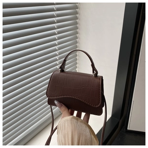 Détail de la texture crocodile marron foncé sur un mini sac à main avec bandoulière fine