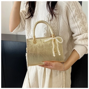 Detail of gold mini square bag with pearl bow charm and round handle for crossbody wear