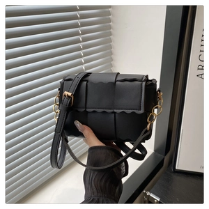 Detail of black woven crossbody bag with scalloped edges and gold metal chain hardware