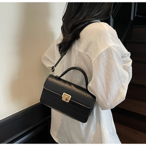 Detailed view of black crocodile pattern leather bag with metallic square lock on model