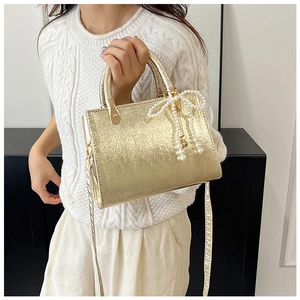 Detail of golden metallic handbag with pearlescent glitter finish and pearl bow charm