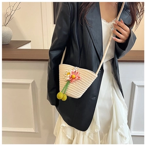 Detail der beigen Strohtasche mit handgestrickten Blumenanhängern und grünen Akzenten