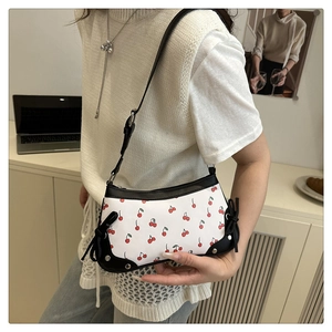 Detail of white underarm bag featuring red cherry prints, black trim, and rivet accents