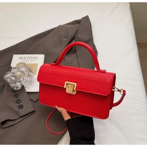 Detail of red crocodile texture handbag with golden buckle and sleek leather finish